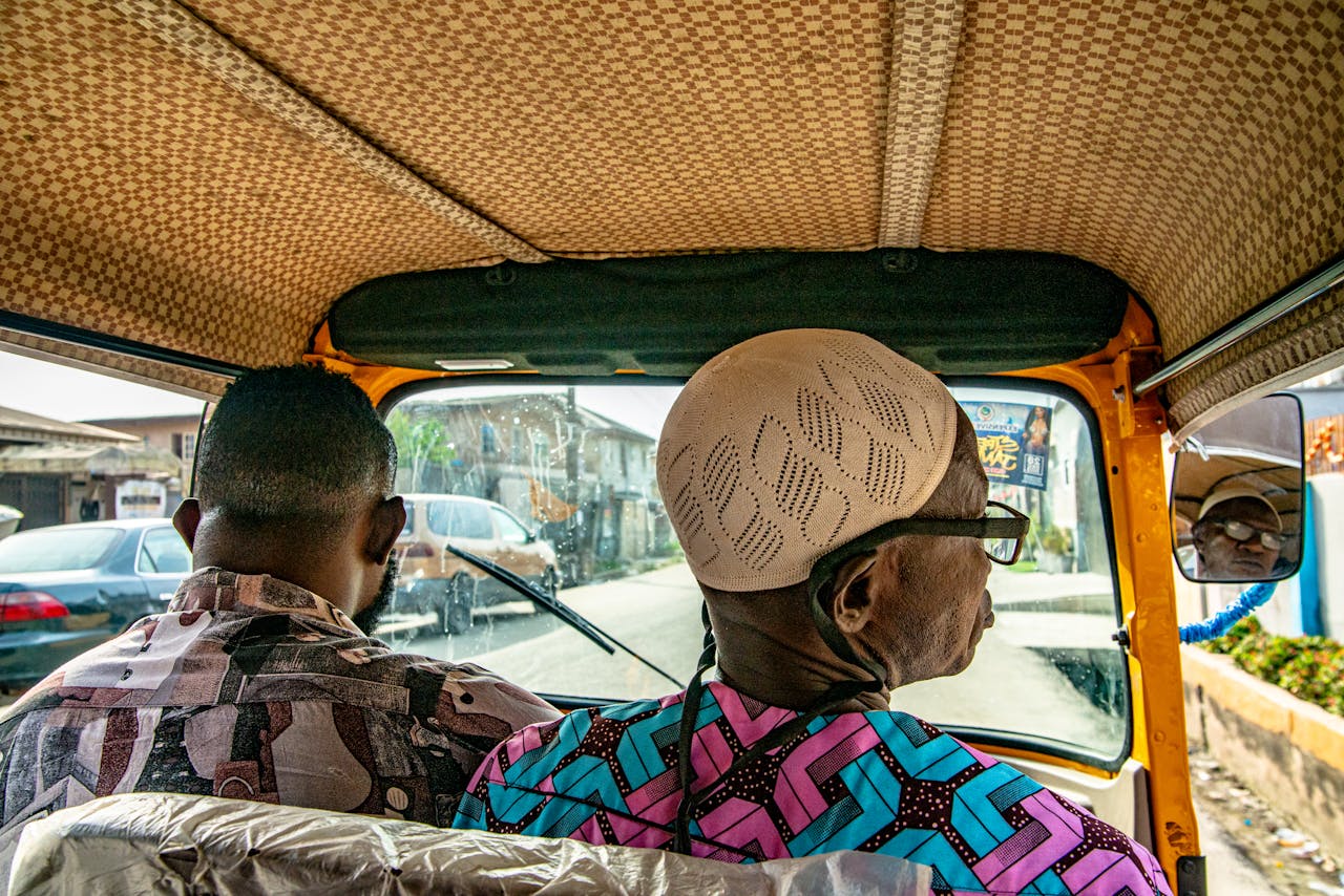 gallery-3 Two men sitting inside a vibrant rickshaw on a sunny day in the city.