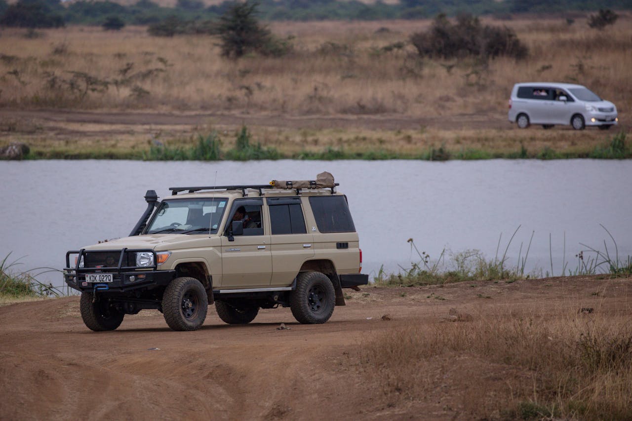 our-services-1 A safari vehicle parked by a serene lake in a vast African savanna landscape.