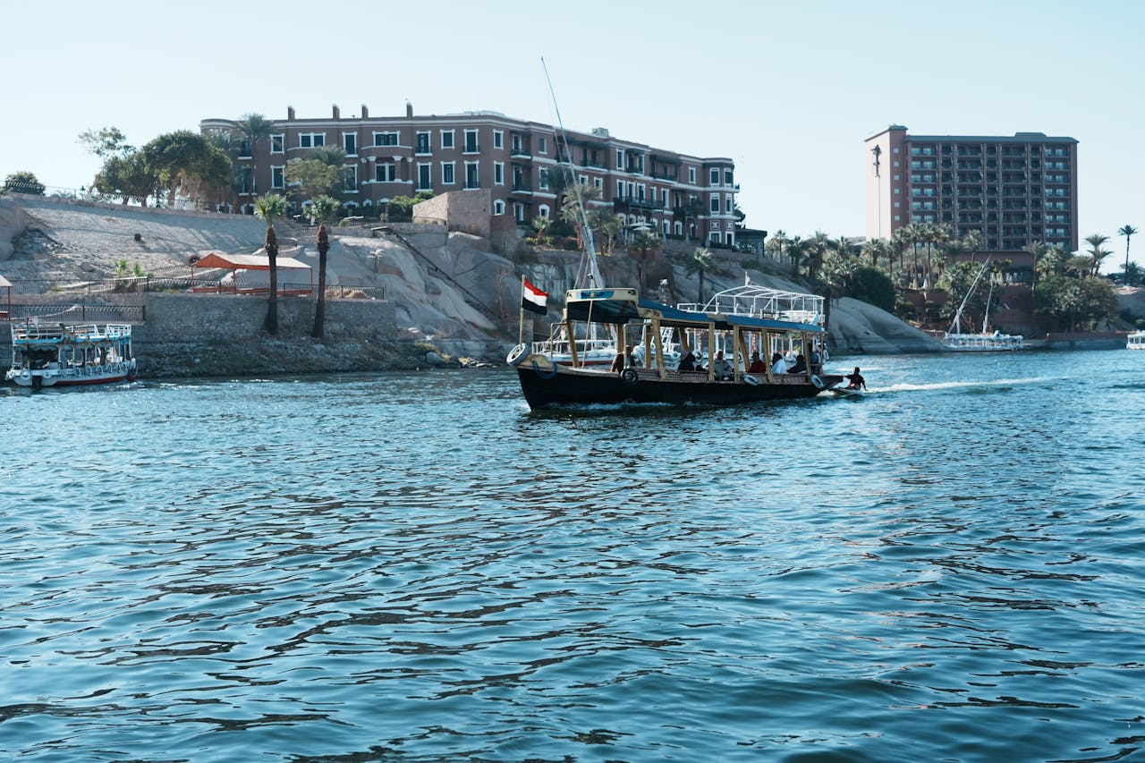 our-services-3 Scenic view of tour boats navigating the Nile River with architectural backdrop in Aswan, Egypt.
