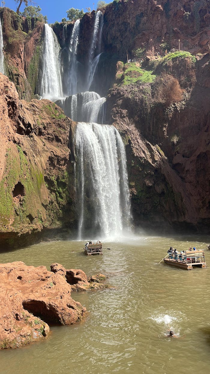 about-01 Capture of Ouzoud Waterfalls with tourists enjoying boat rides under the bright sun.